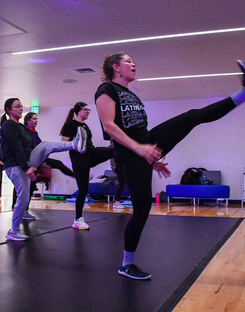 Woman kicking up in the air teching a class.