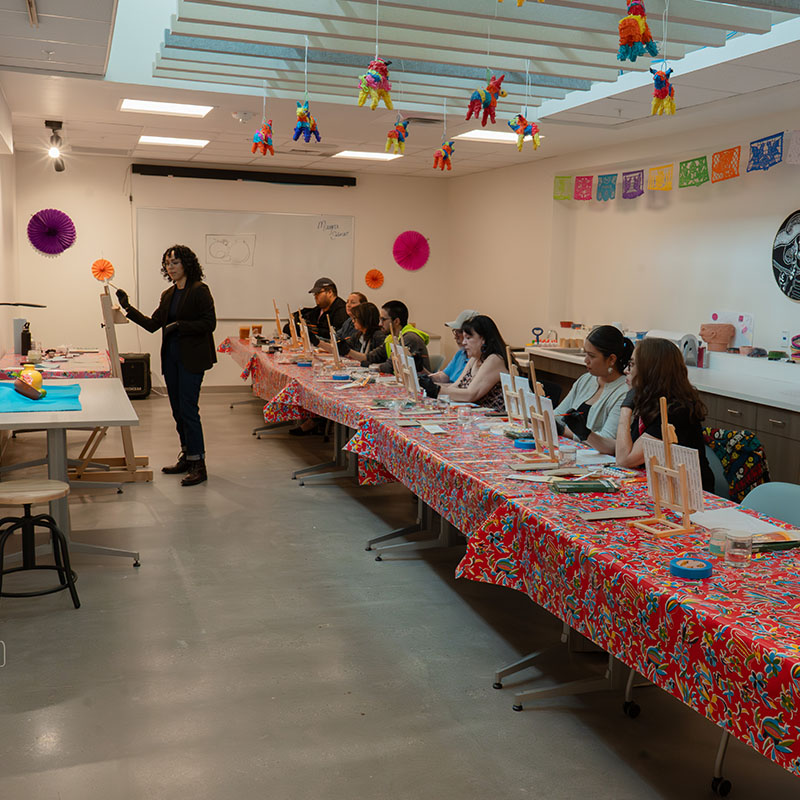 People at a long table painting on canvases.