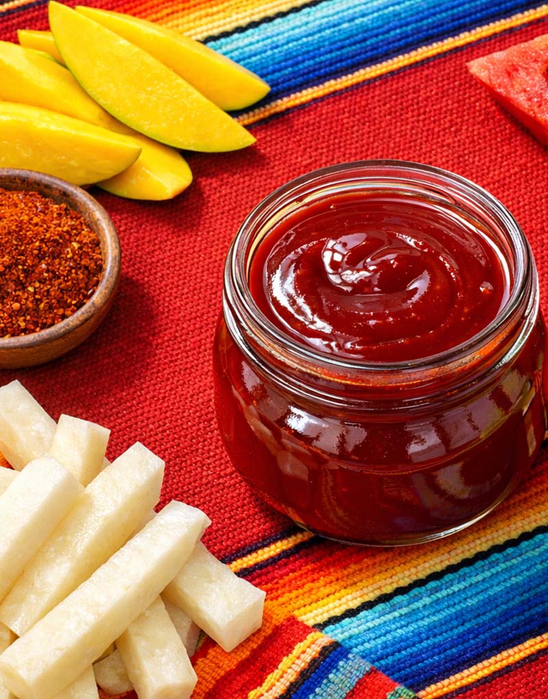 Jar of chamoy surrounded by mango slices.